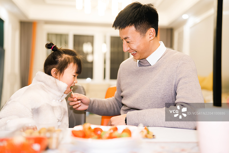 快乐的年轻亚洲父亲在家里喂他的女儿吃东西图片素材