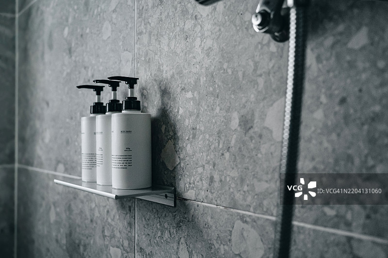 现代时尚浴室中，金属架上摆放着沐浴露、洗发水和护发素，墙面铺有灰色瓷砖。浴室内有浴室配件套装和身体护理套件，体现了家庭身体护理、美容、护肤和健康生活方式的理念。图片素材