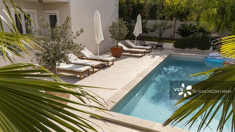 现代游泳池，配有白色躺椅和棕榈树，位于豪华度假租赁花园中图片素材