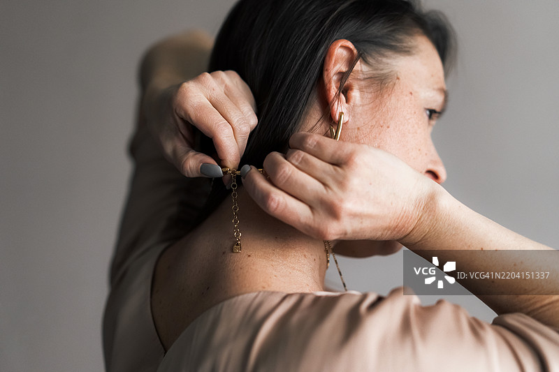 一位女性试图系紧链锁，珠宝。老年人的个性与风格。从背面拍摄，中景。图片素材