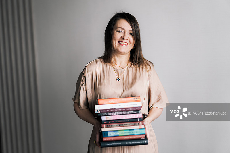手握一堆书籍的快乐女性肖像。成年学生、教练、自我发展、自我意识的概念。图片素材