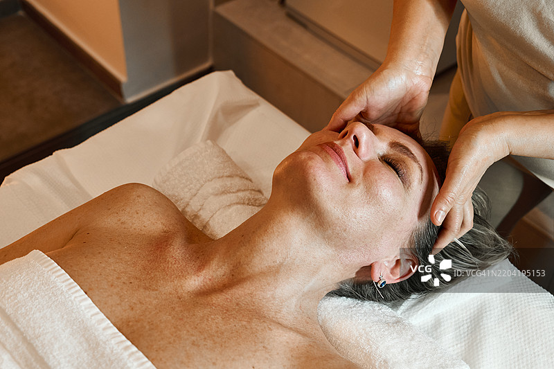 中年女性在水疗沙龙享受头部按摩，放松身心。图片素材