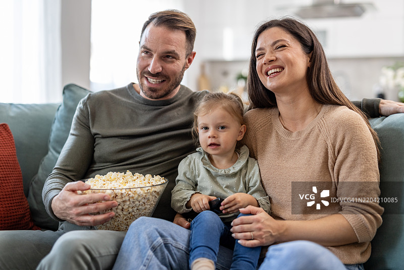 快乐的家庭在沙发上看电视，吃着爆米花图片素材