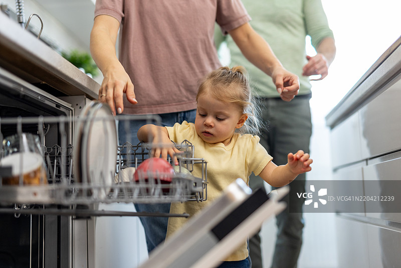 好奇的幼儿在现代厨房里帮助父母卸洗碗机图片素材