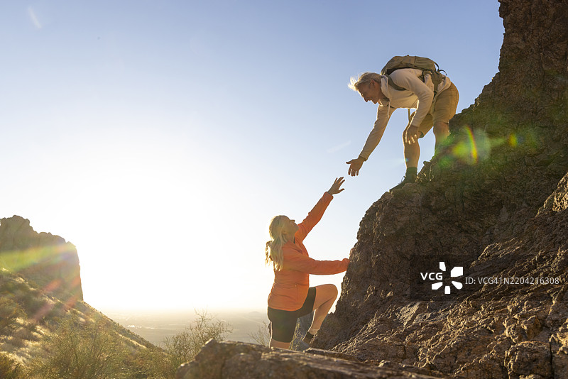 在日落时分，登山者在沙漠中伸出援手图片素材