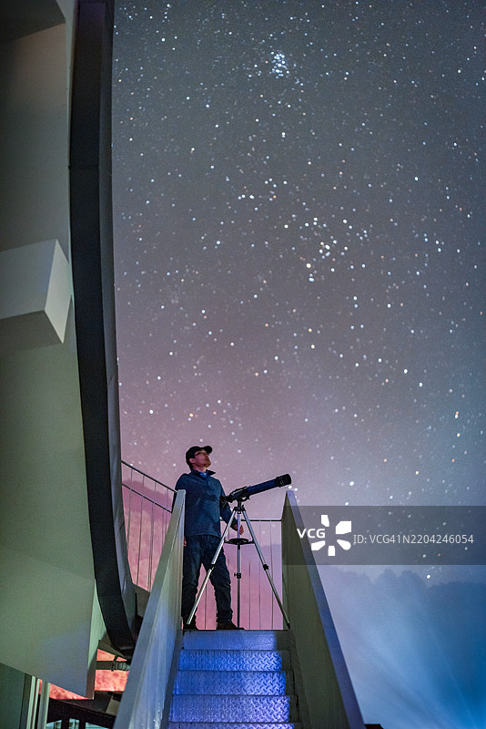 天文爱好者站在望远镜旁，凝视着星空。图片素材