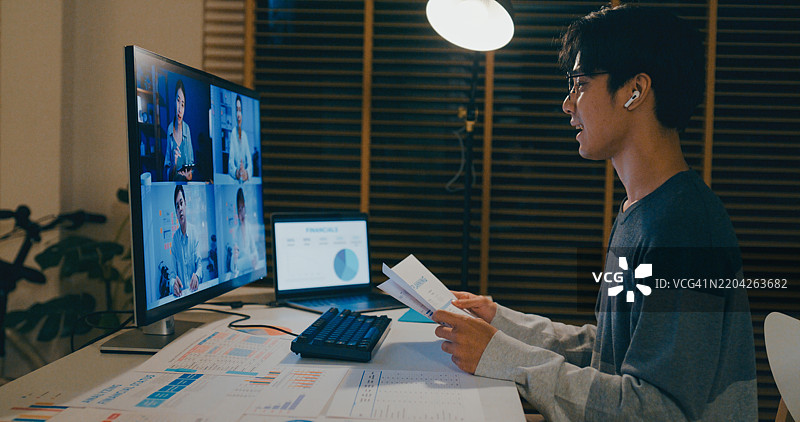 年轻的亚洲人在家办公室深夜进行视频会议，讨论财务文件，与同事在线交流，展示远程团队合作和奉献精神。远程工作与财务。图片素材