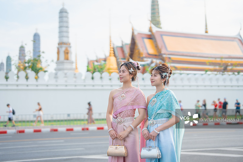 两位年轻美丽的亚洲女性身着传统泰国服饰，愉快而令人印象深刻地游览位于泰国曼谷的阿伦寺。图片素材