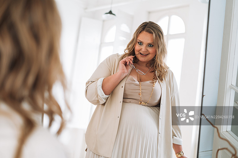 自信的年轻女性在镜子前欣赏自己，身材丰满。图片素材