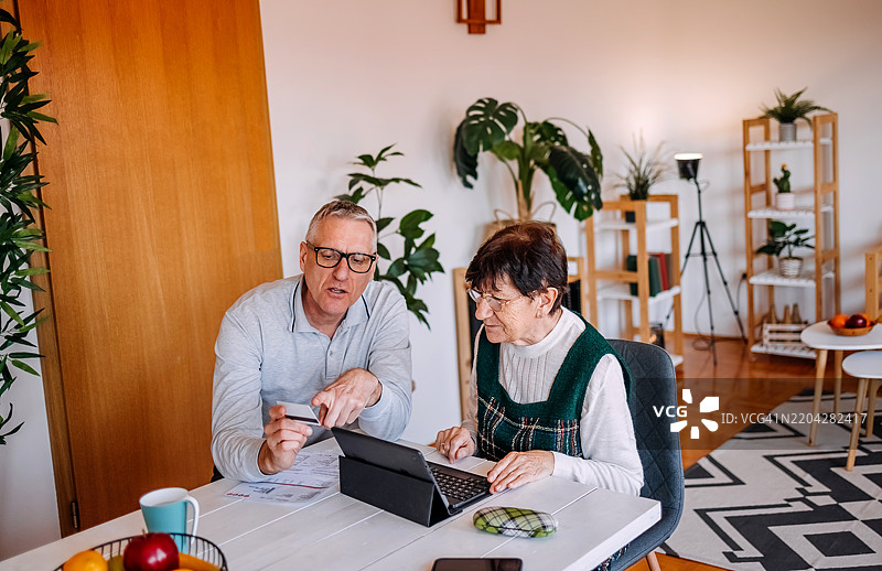 在家与老年人共度时光，教他们如何使用笔记本电脑和平板电脑支付账单图片素材