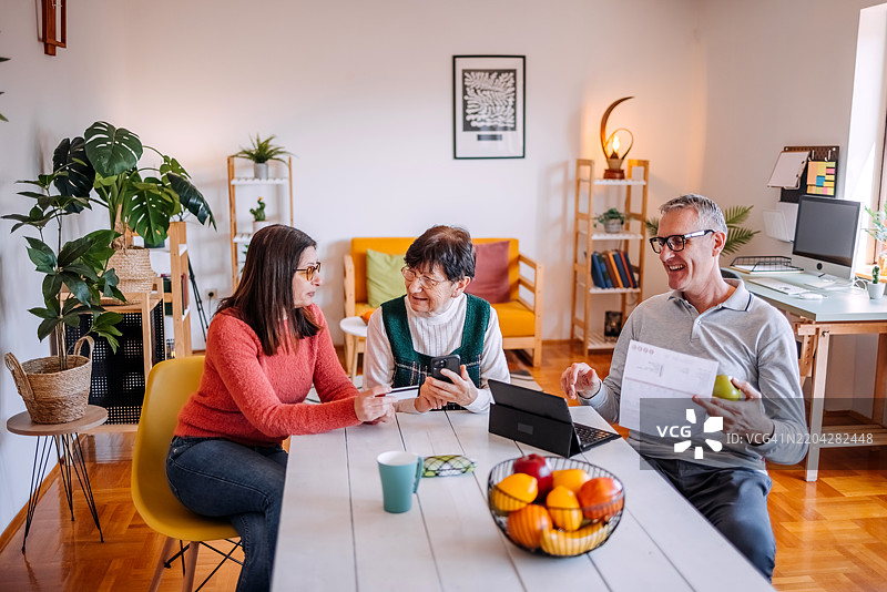 在家与老年人共度时光，教他们如何使用笔记本电脑和平板电脑支付账单。图片素材