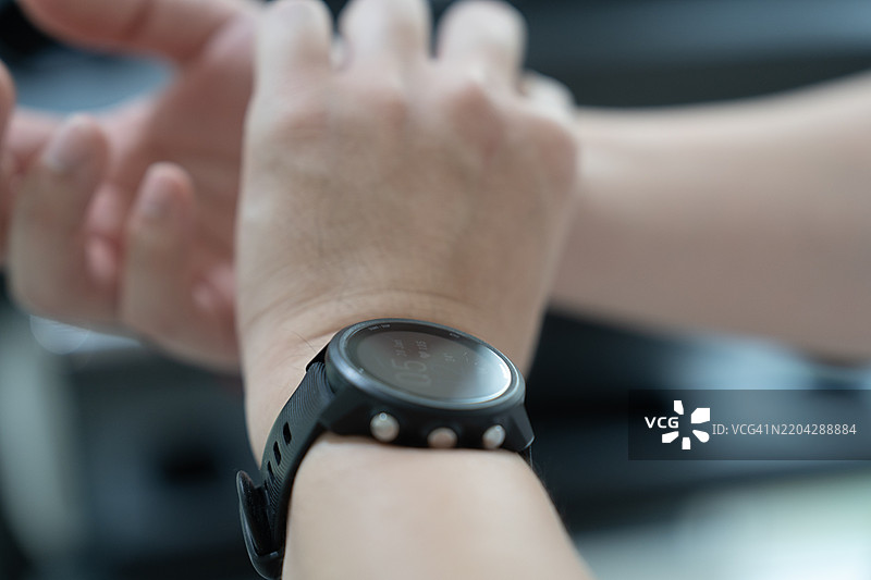 在健身房里，一个人戴着黑色智能手表，正在仔细检查自己的脉搏。图片素材