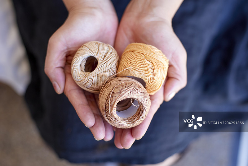 女人手中拿着三卷米色纱线图片素材