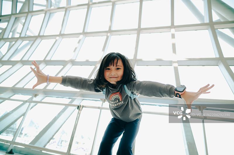 在机场，活泼的小女孩微笑着，享受着旅行前的乐趣。图片素材