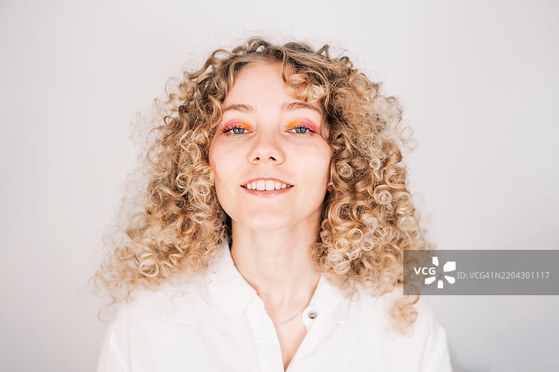 微笑的金发卷发女性肖像，穿着白衬衫图片素材