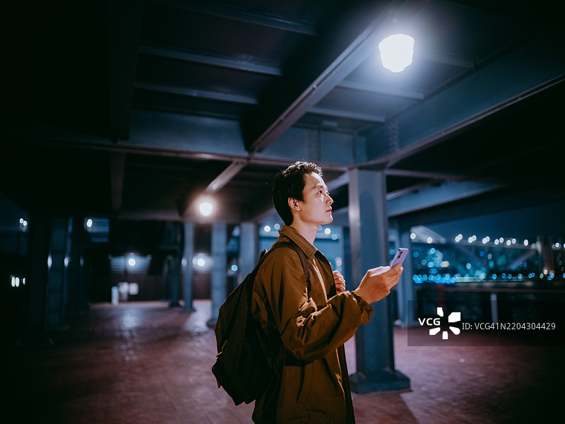 一位年轻的亚洲男子站在钢结构建筑下使用智能手机图片素材