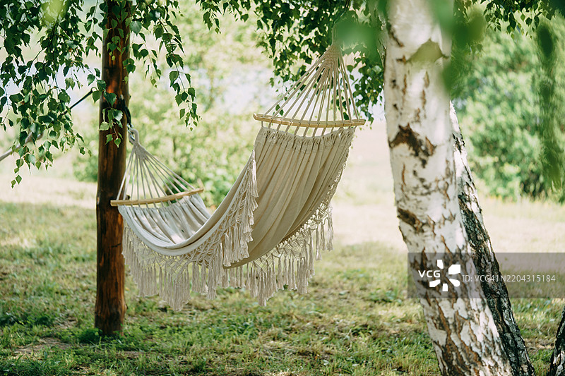 空荡荡的吊床悬挂在树间，宁静的花园中邀请人们放松身心。图片素材