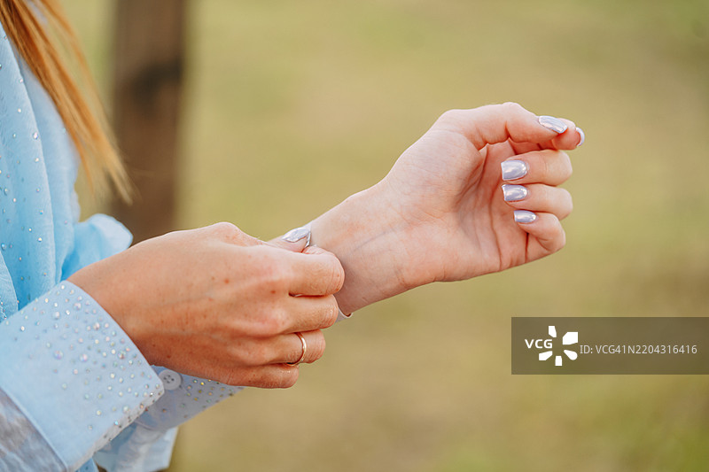 女人在自然中调整带有精致指甲的手链图片素材