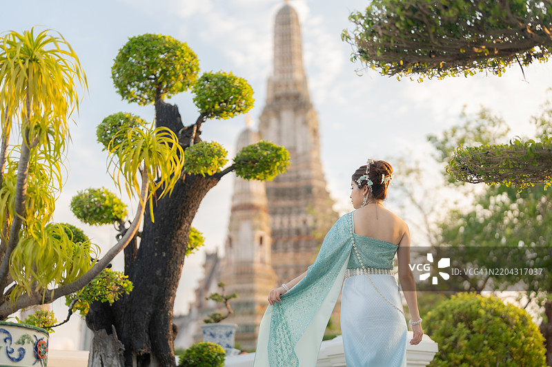 在泰国曼谷的黎明寺，穿着传统泰国服装的年轻亚洲女性在日落时分被拍摄。图片素材