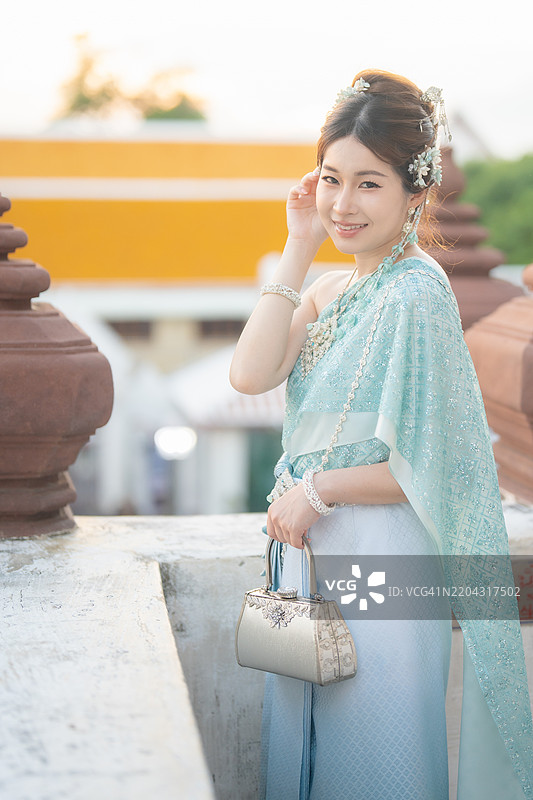 年轻的亚洲女性身着华丽的泰国传统服饰，在黎明寺（阿伦寺）展现出优雅与文化自豪感。图片素材