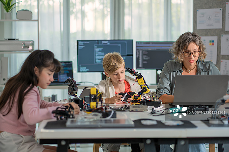 年轻工程师在工作：孩子们在教室里与老师一起学习机器人技术。图片素材