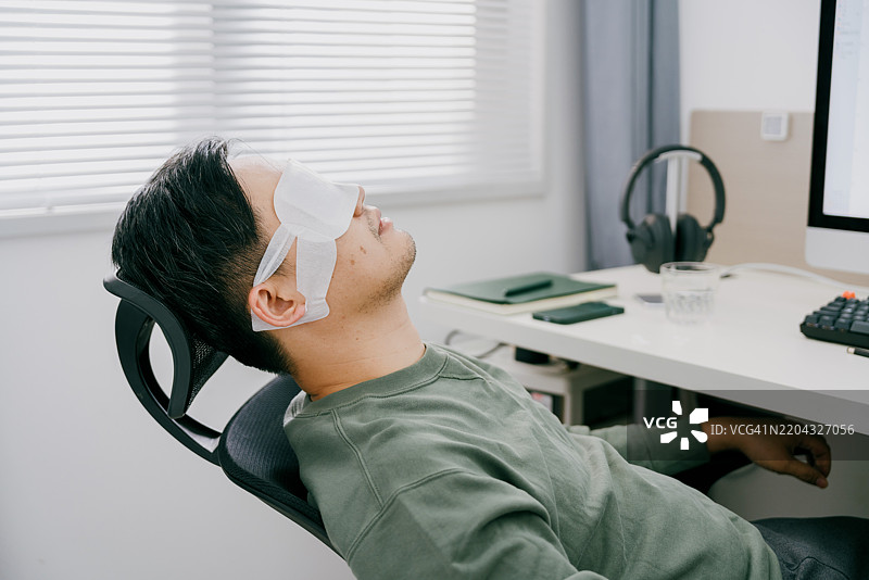 一位亚洲男性在家中放松，使用蒸汽眼罩；亚洲家庭健康管理实践图片素材