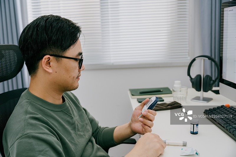 一位亚洲男性在家中使用仪器测量尿酸；亚洲家庭健康管理实践图片素材