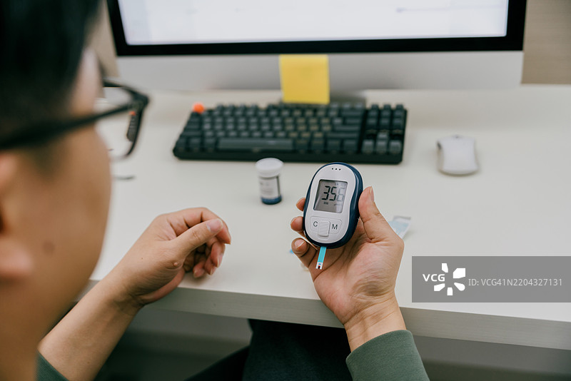 一位亚洲男性在家中使用仪器测量尿酸；亚洲家庭健康管理实践图片素材