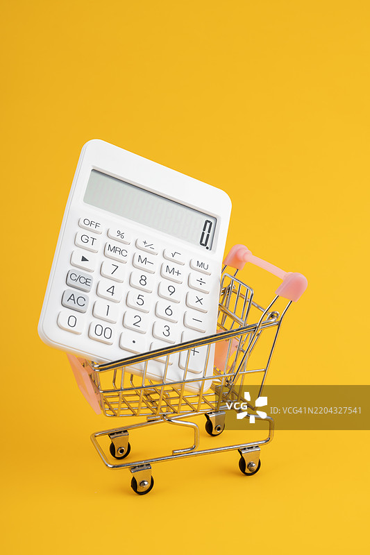 黄色背景上的购物车里的白色计算器。图片素材