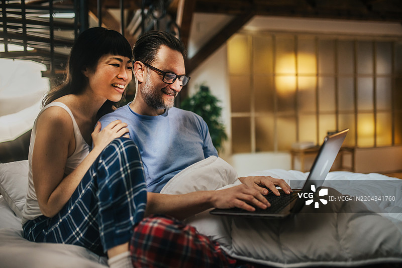 美丽的情侣坐在床上使用笔记本电脑工作。图片素材