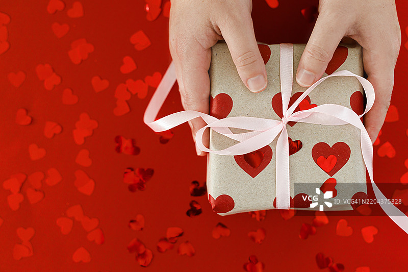 情人节快乐 时尚礼品盒手握着，红色心形和粉色蝴蝶结在红色背景上平铺 爱的背景，留白空间图片素材