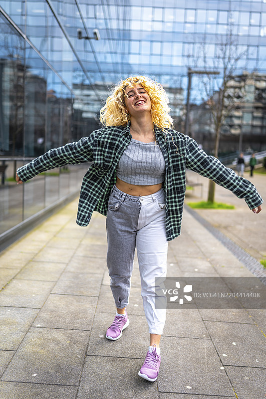 无忧无虑的年轻女性在现代城市环境中享受城市音乐，张开双臂跳舞，脸上洋溢着快乐的表情。图片素材