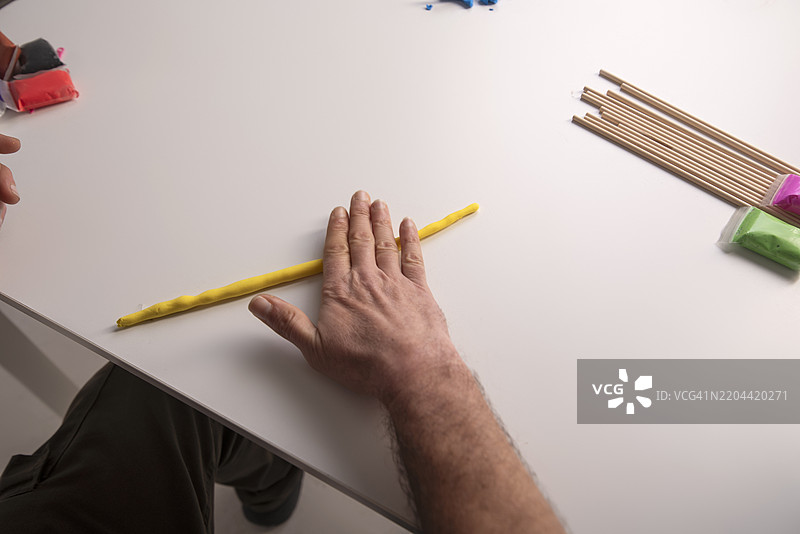 一只手在白色桌子上捏制塑料泥和彩色粘土的手工艺品图片素材