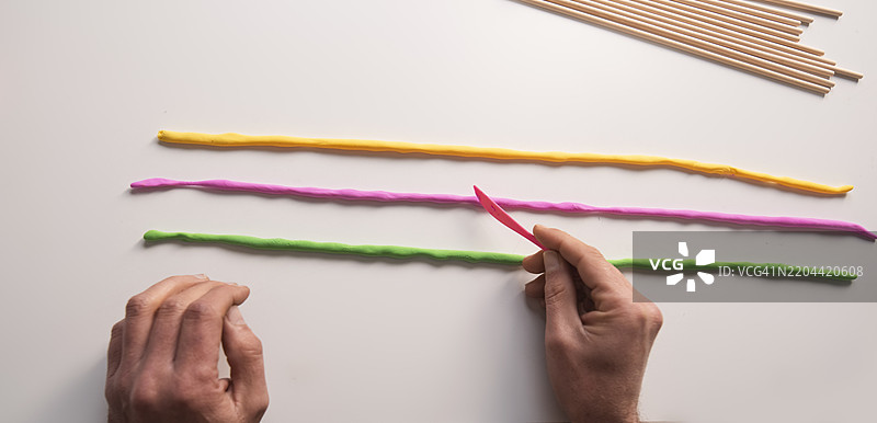 在白色背景上，桌子上的手正在捏制彩色粘土的横幅广告图片素材