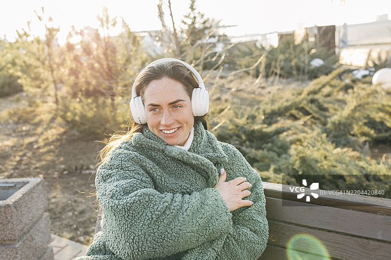 春天里美丽的女人坐在长椅上，享受生活，戴着无线耳机听音乐。图片素材