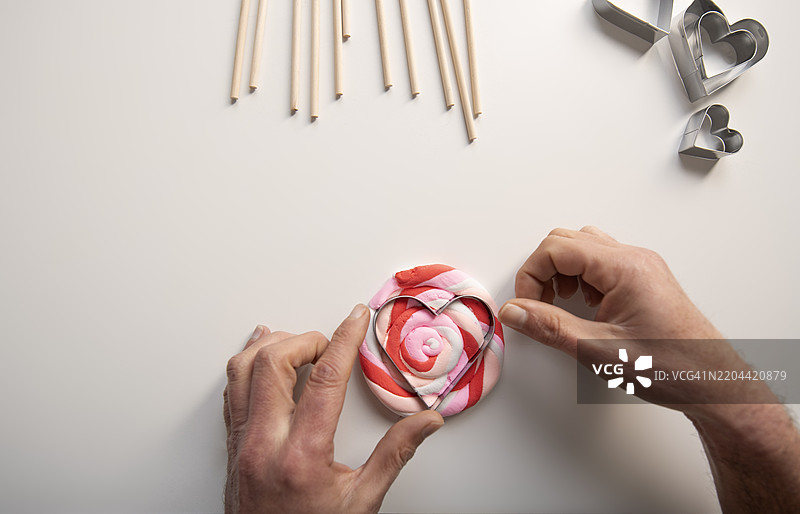 用粘土制作情人节礼物的手，正在用模具塑形一个心形。图片素材