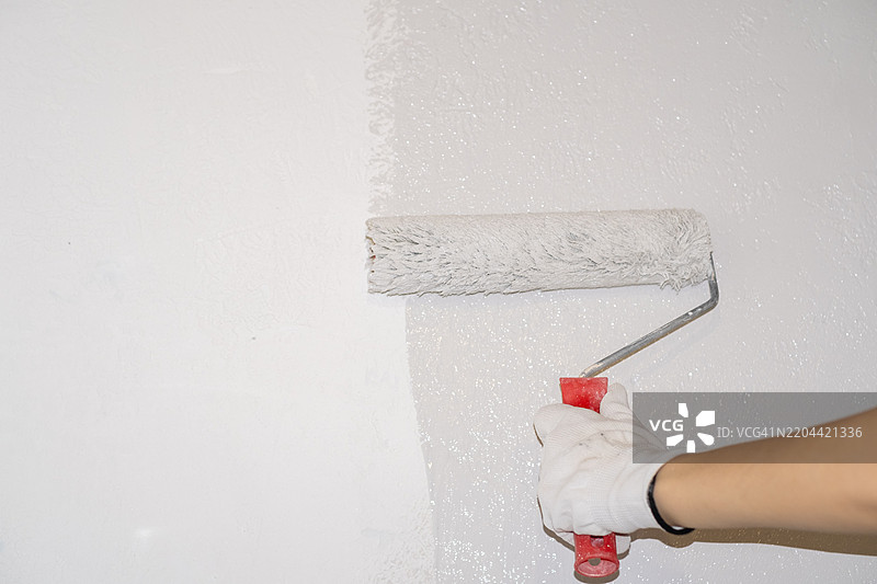 一位女性正在用滚筒手动涂刷墙壁，正在粉刷公寓。图片素材