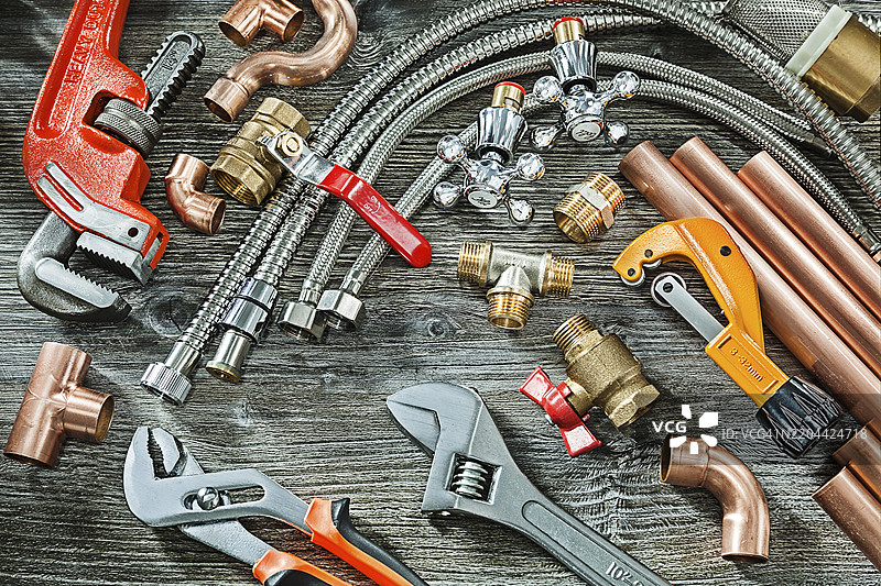 管道概念，大量管道配件，猴子和可调扳手，铜和黄铜接头，管子切割器，背景为复古木材。图片素材