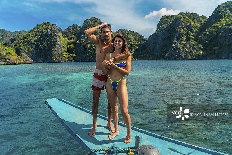 一对情侣站在传统的菲律宾船上，拥抱着，享受着菲律宾科隆岛的壮丽风景。图片素材