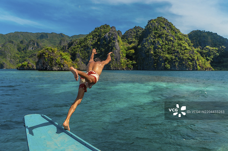 年轻男子从菲律宾科隆岛的传统班卡船跳入碧蓝的海水中，享受东南亚的夏日假期图片素材