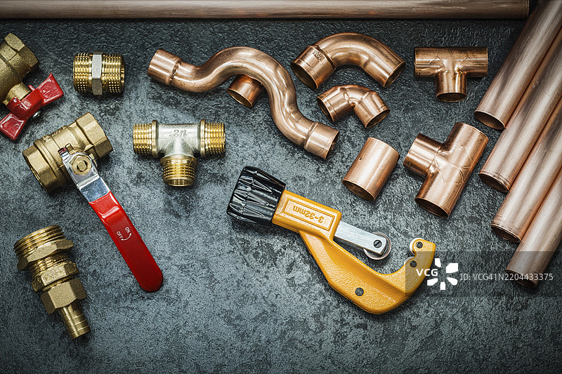 黑色背景上的管道工工具、铜管、配件、管子切割器和阀门图片素材