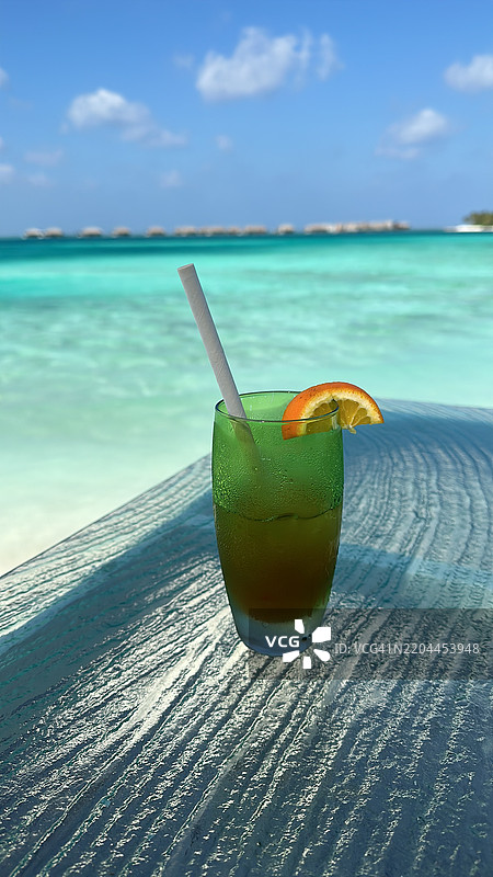 清爽的热带饮品，橙片放在玻璃桌上，俯瞰马尔代夫的海景图片素材