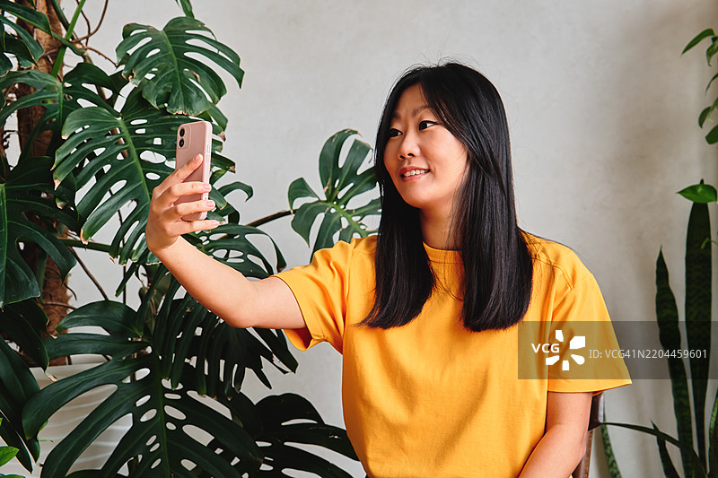 美丽的亚洲女性在热带植物中拍摄自拍，阳光明媚。图片素材