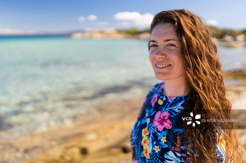 美丽的女人站在岩石海滩上，欣赏海景。她穿着潜水服，准备进行自由潜水。图片素材