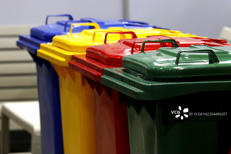 一排垃圾桶。垃圾桶的颜色各异，包括绿色、蓝色、红色和黄色。图片素材