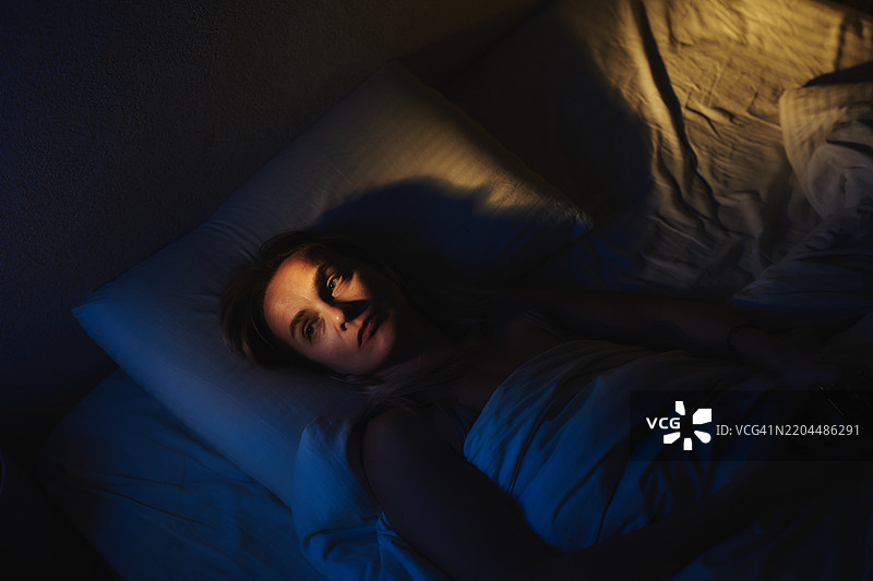 女人在床上醒着，灯光效果戏剧化图片素材