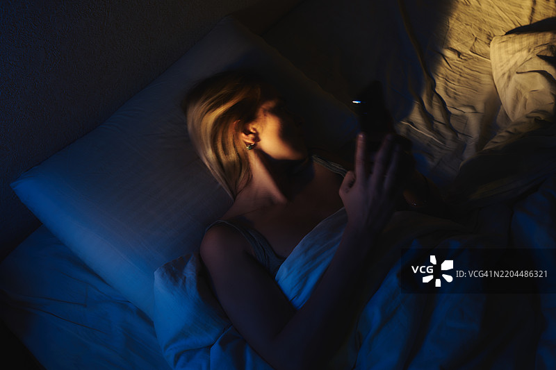 晚上躺在床上使用智能手机的女人图片素材