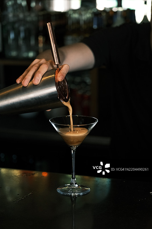 调酒师在时尚酒吧将新鲜摇匀的浓缩咖啡马提尼倒入经典酒杯，咖啡风味鸡尾酒的调制，专业调酒和手工鸡尾酒体验图片素材