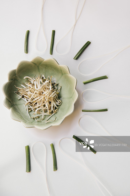 新鲜绿豆芽特写，放在绿色陶瓷碗中，体现有机健康食品概念，白色背景上方有青葱，亚洲料理食材。图片素材