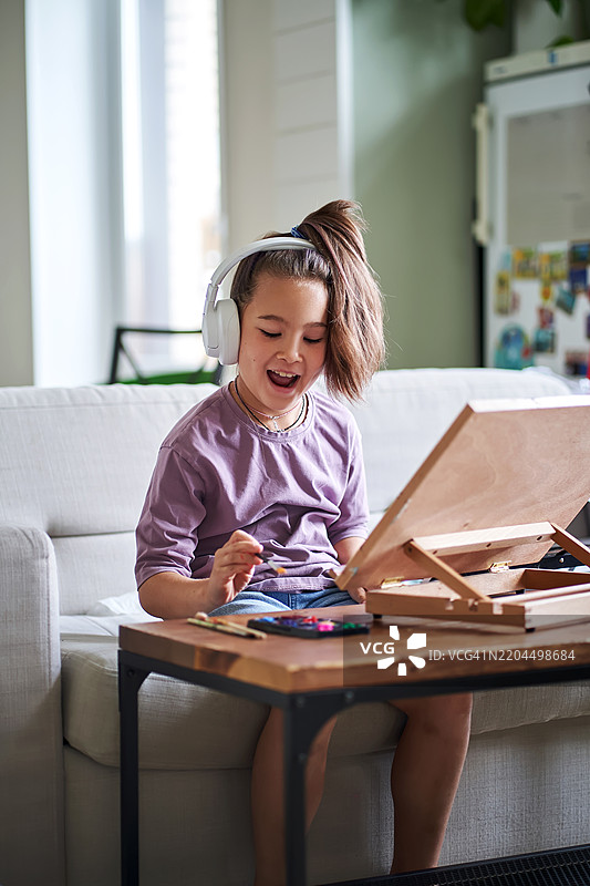 一个戴着耳机的女孩坐着在桌子上画画。图片素材